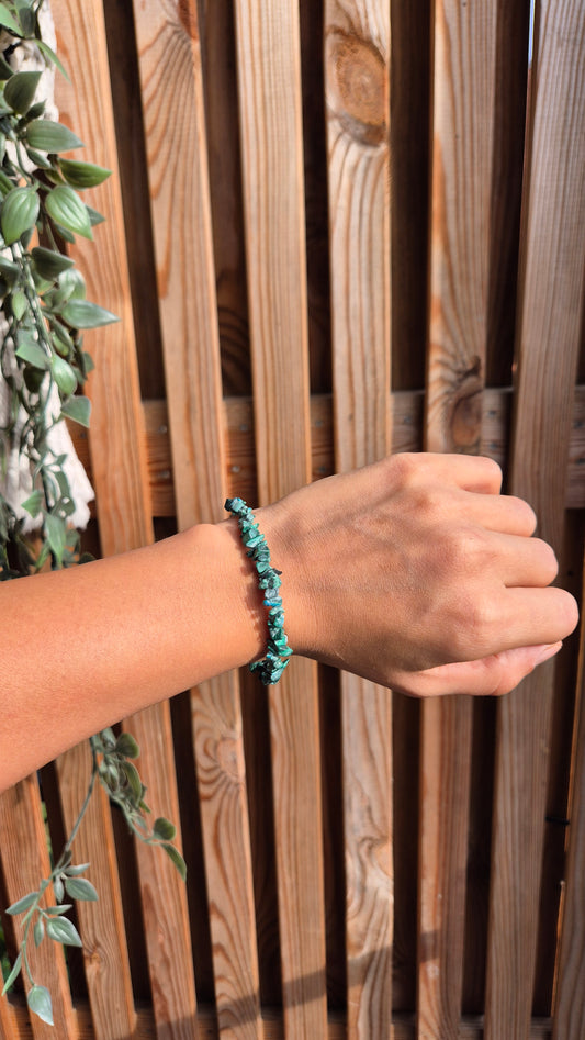 A turquoise beaded bracelet worn on a person's wrist, shown against a wooden slat fence background with green foliage on the left.