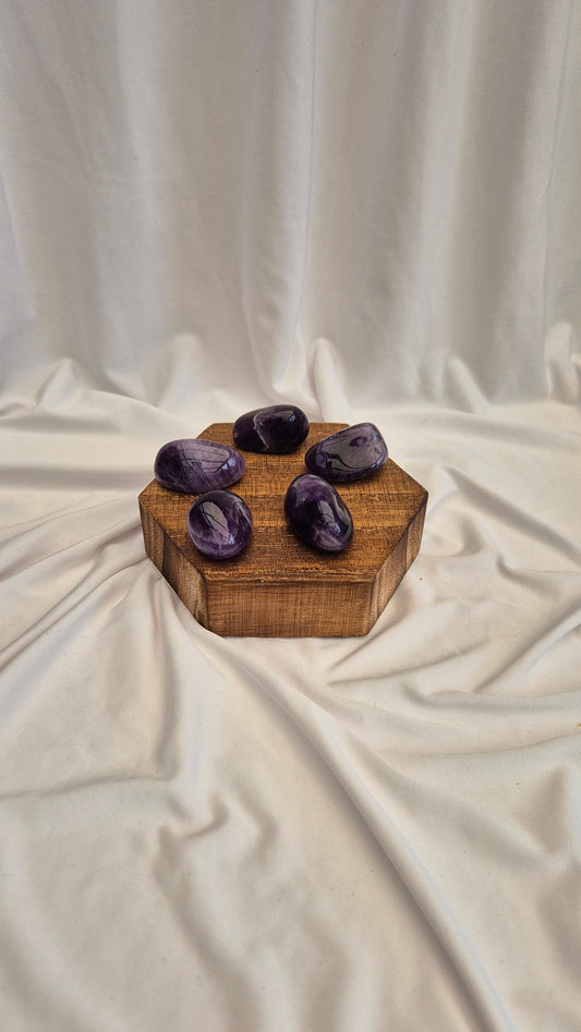 Five purple stones on a wooden hexagonal block against a white curtain background