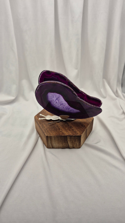 A purple agate slice wall art piece displayed on a rustic wooden block stand, set against a draped white fabric backdrop.