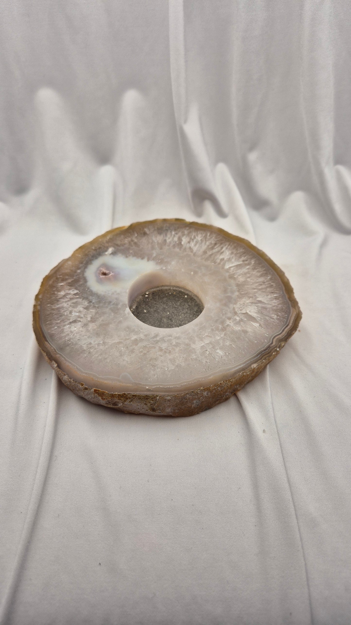 A polished natural agate stone ring plate with a central hole, resting on draped white fabric.
