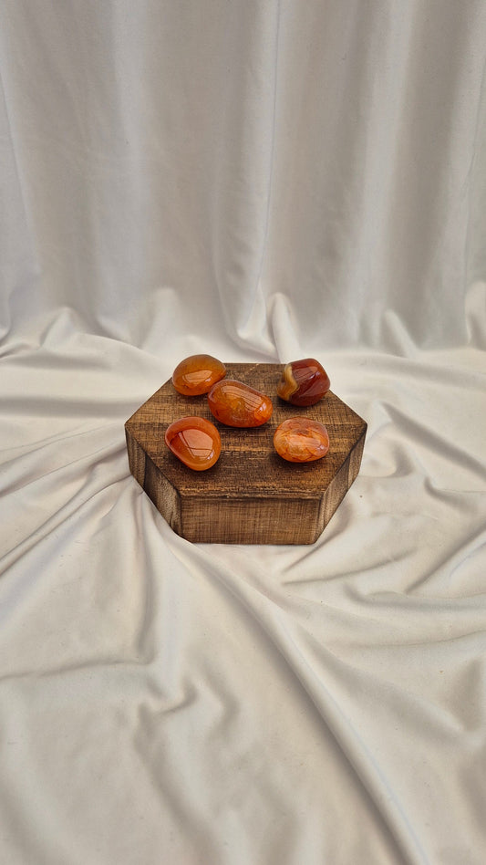 Five orange stones on a wooden hexagonal block against a white fabric background