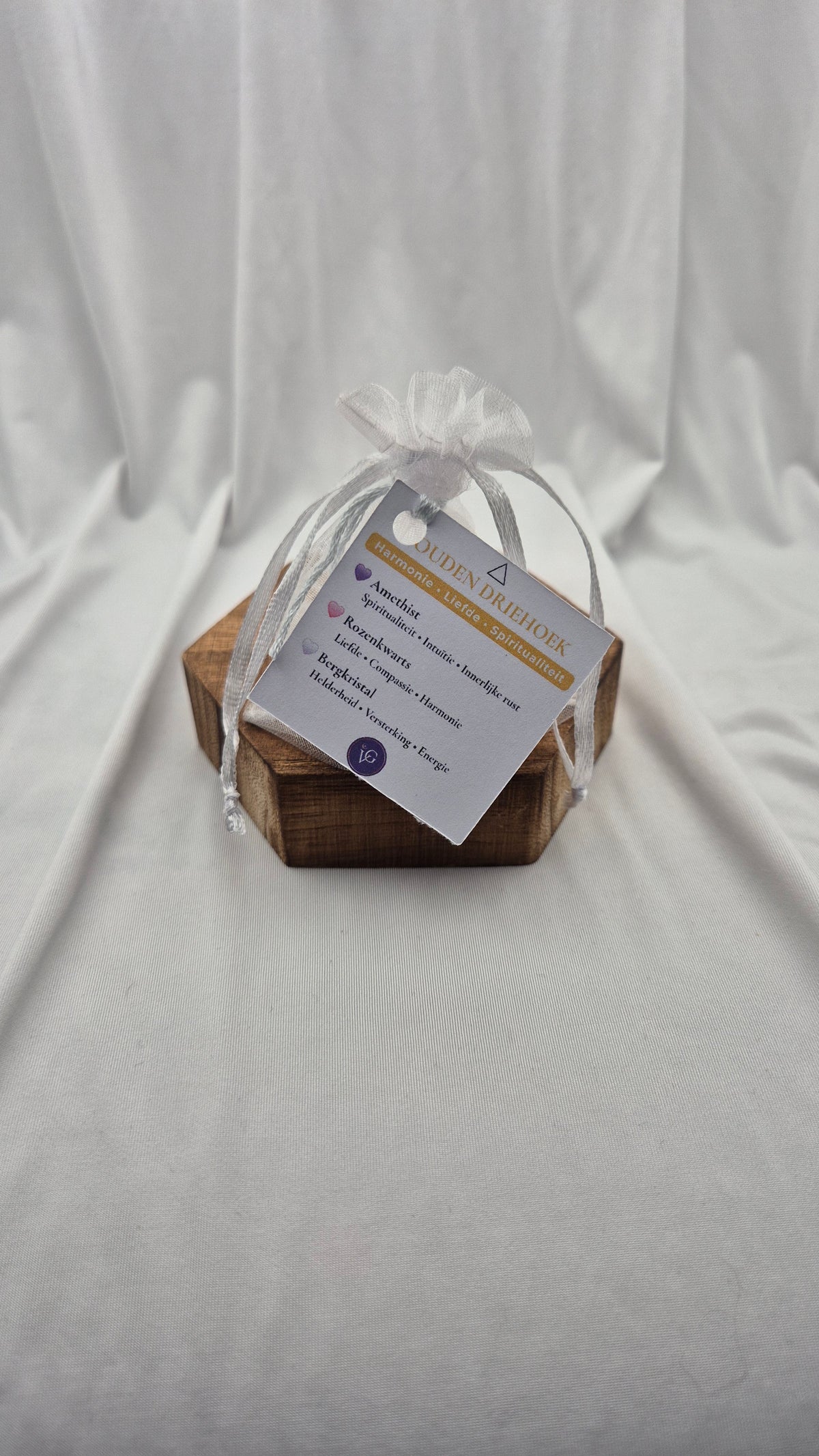 A small wooden keepsake box wrapped in a sheer white ribbon and a paper tag, photographed against draped white fabric.