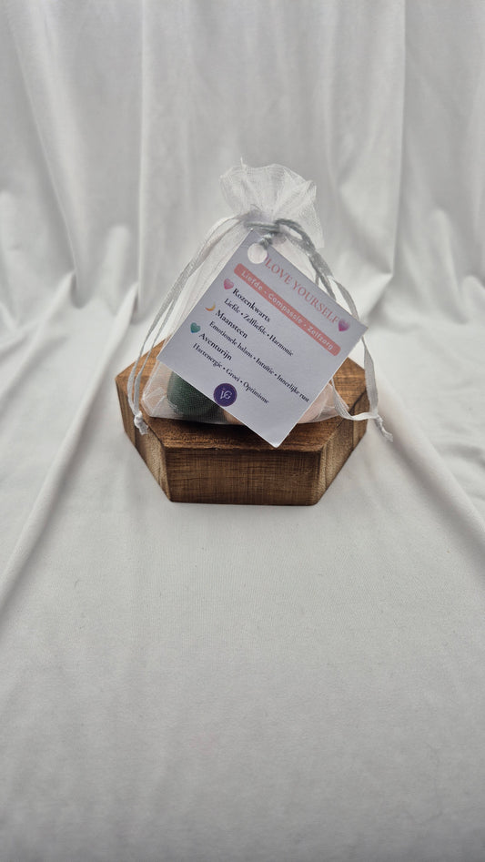 A small wooden hexagonal box holding a wrapped gift tied with a sheer white bag and a printed tag, set against a draped white fabric backdrop.