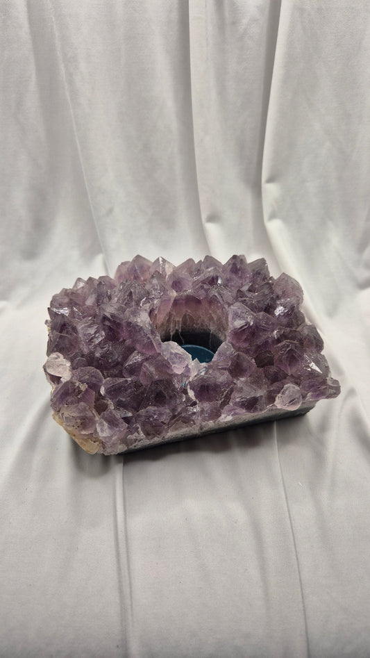 A raw amethyst crystal cluster geode with a hollow center, resting on a white draped fabric background.