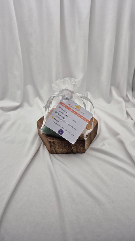 A small gift set in a hexagonal wooden box on a draped white fabric background. The set includes a clear cellophane bag with a white ribbon and a printed tag.