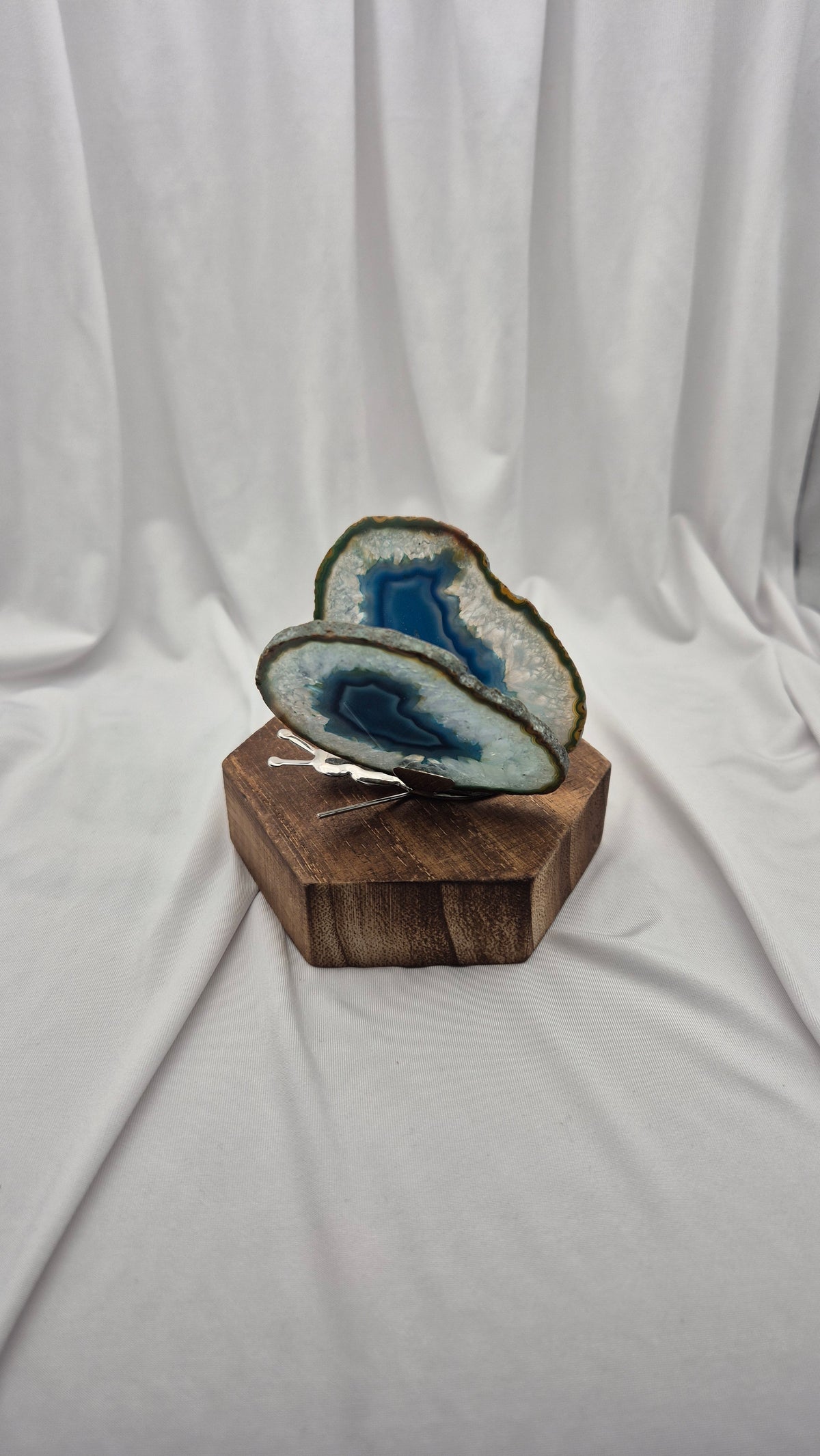 Two polished agate geode slices with blue and white patterns, displayed on a hexagonal wooden block against a draped white fabric background.