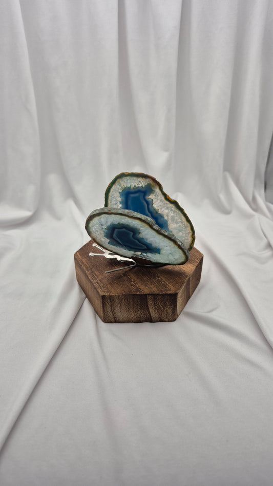 Two polished agate geode slices with blue and white patterns, displayed on a hexagonal wooden block against a draped white fabric background.