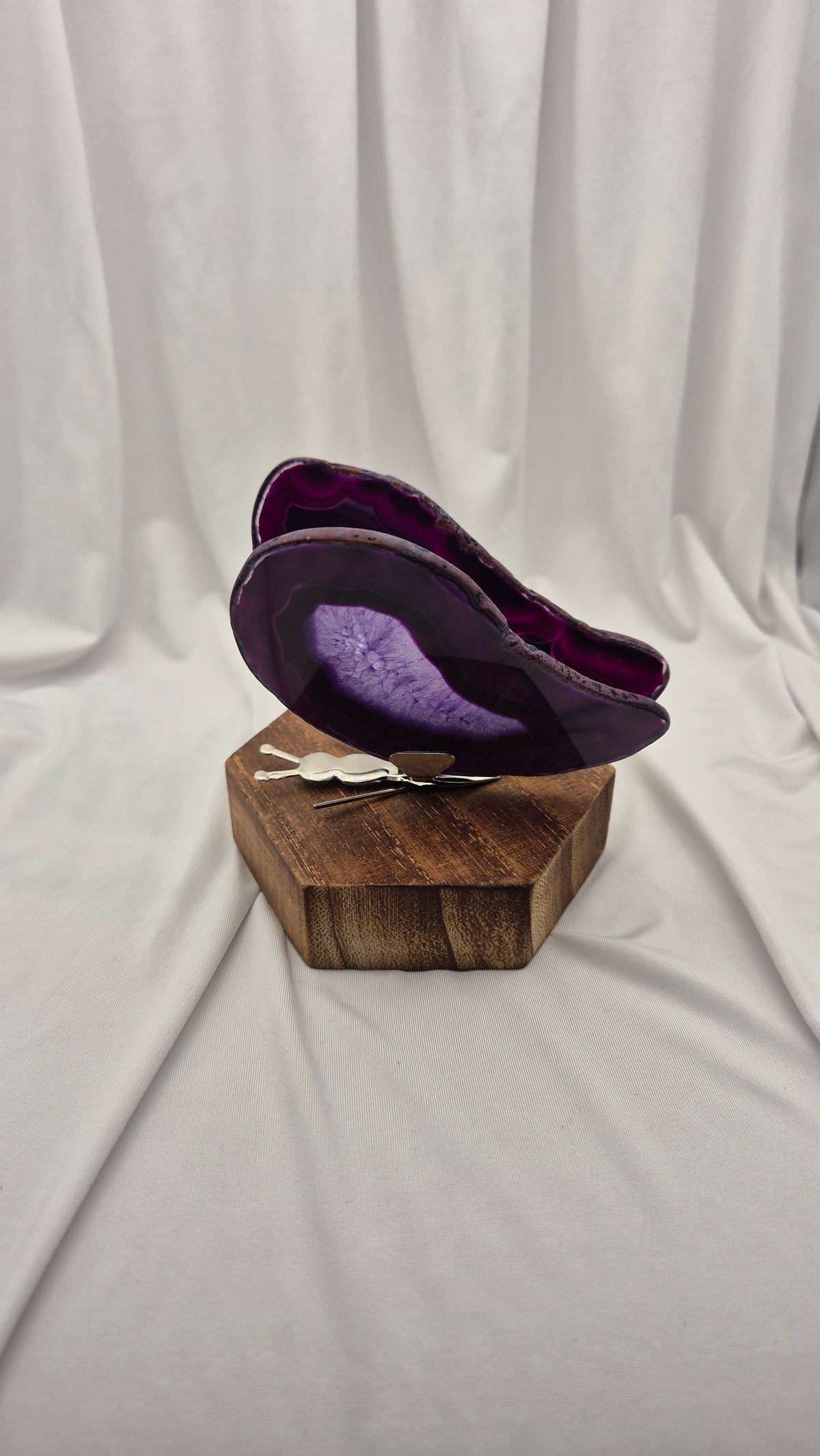 A purple agate slice wall art piece displayed on a rustic wooden block stand, set against a draped white fabric backdrop.