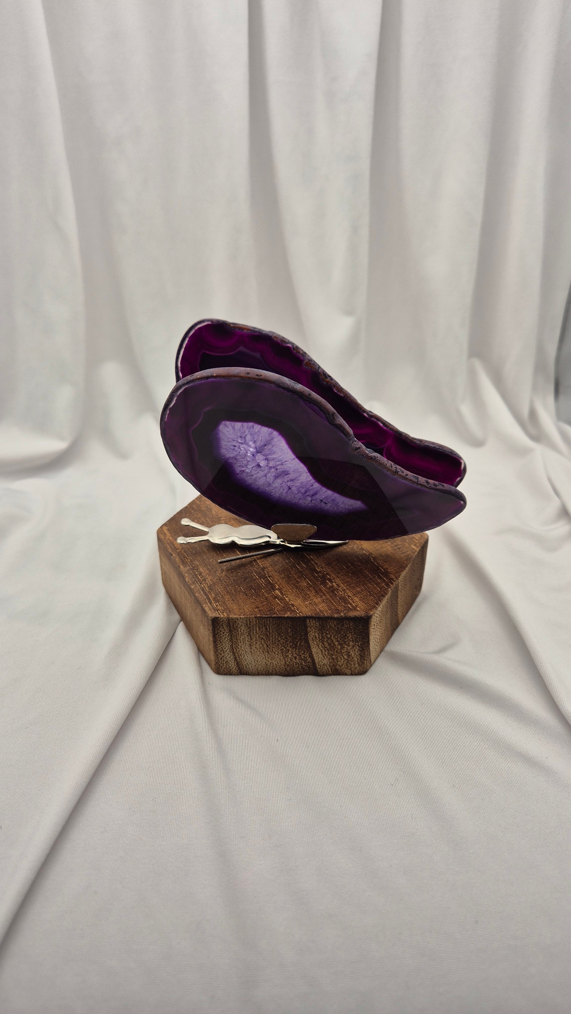 A purple agate slice wall art piece displayed on a rustic wooden block stand, set against a draped white fabric backdrop.