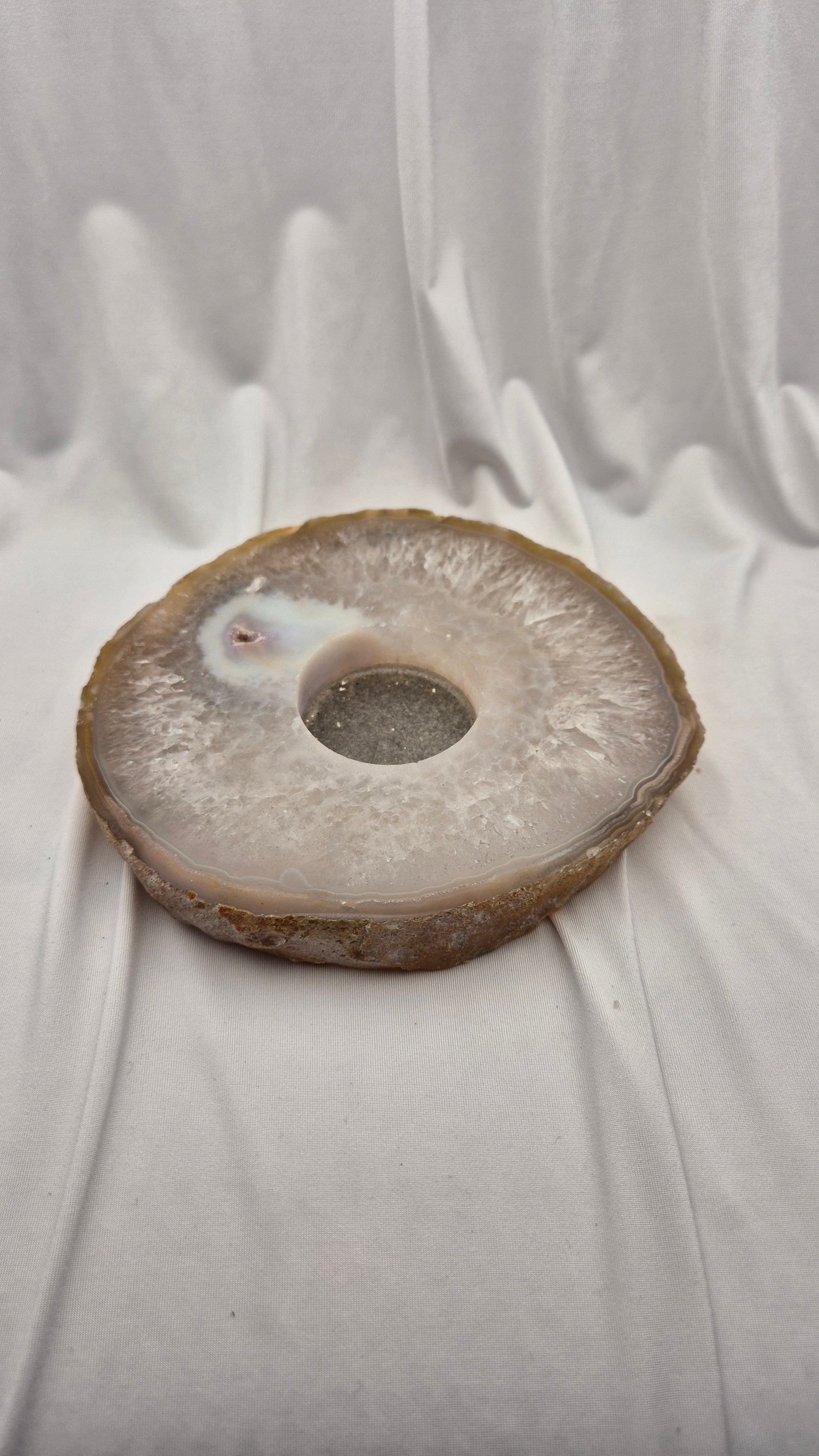 A polished natural agate stone ring plate with a central hole, resting on draped white fabric.