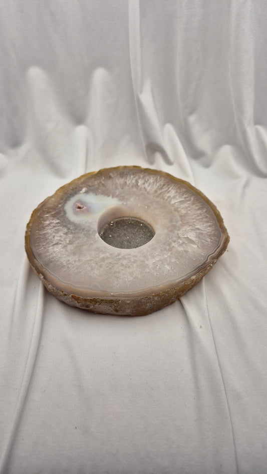 A polished natural agate stone ring plate with a central hole, resting on draped white fabric.