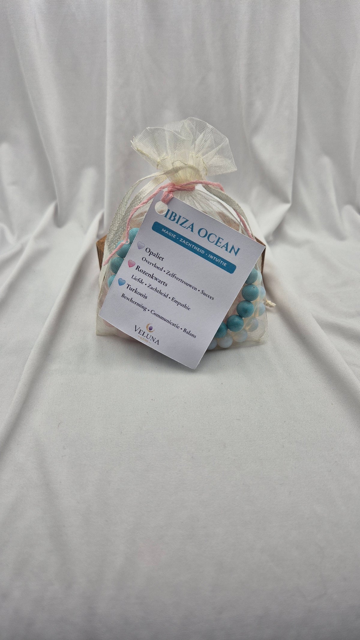 A small clear mesh bag containing a beaded strand tied with a sheer ribbon, with a white product tag reading 'IBIZA OCEAN' and 'VALLI' at the bottom, placed on a white fabric backdrop.