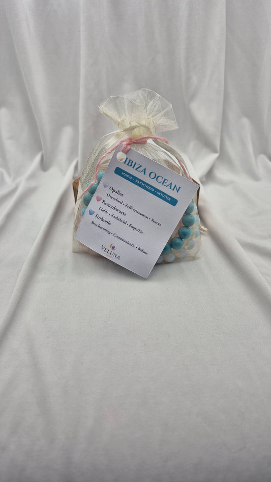 A small clear mesh bag containing a beaded strand tied with a sheer ribbon, with a white product tag reading 'IBIZA OCEAN' and 'VALLI' at the bottom, placed on a white fabric backdrop.