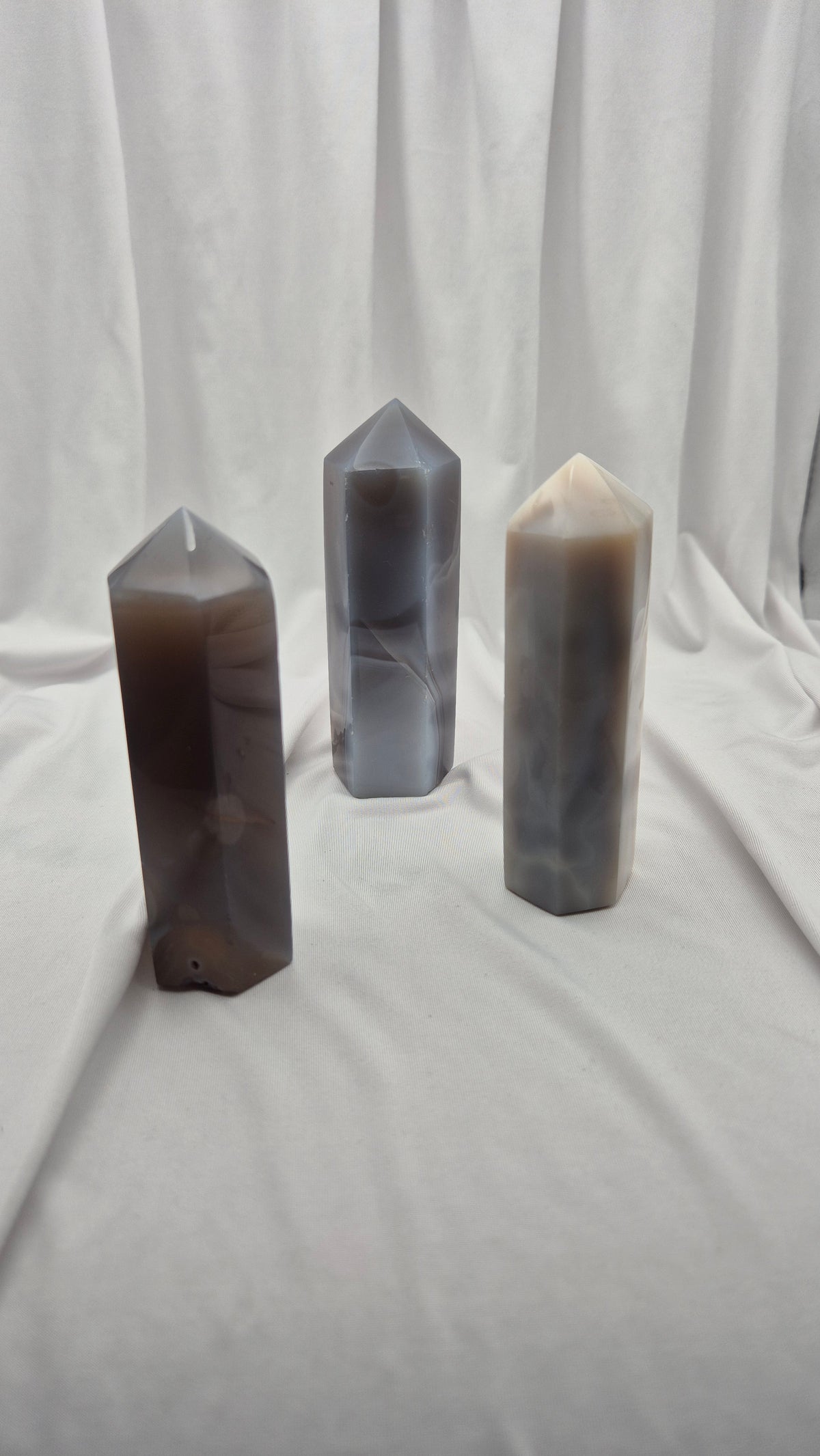 Three polished crystal point towers in natural stone colors, standing upright on a draped white fabric backdrop.