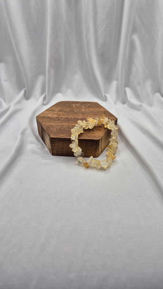 A beaded stretch bracelet made of irregular, translucent pale yellow and cream stones, draped over a small hexagonal wooden box on a draped white fabric background.