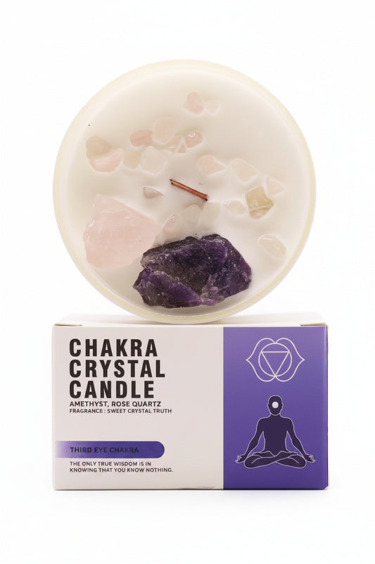 Chakra Crystal Candle in a round white wax candle with embedded crystals, shown above its white and purple retail box. The candle includes rose quartz, amethyst, and green aventurine crystals, with a small copper needle element.