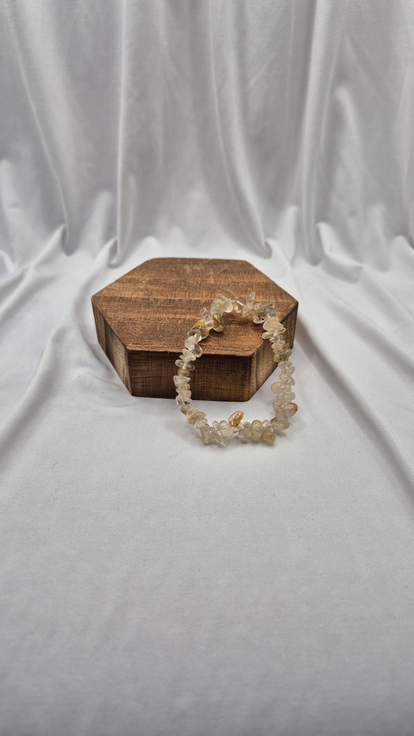 A beaded stretch bracelet made of small clear and pale yellow crystal-like beads, draped over a hexagonal wooden jewelry box on a white draped fabric backdrop.