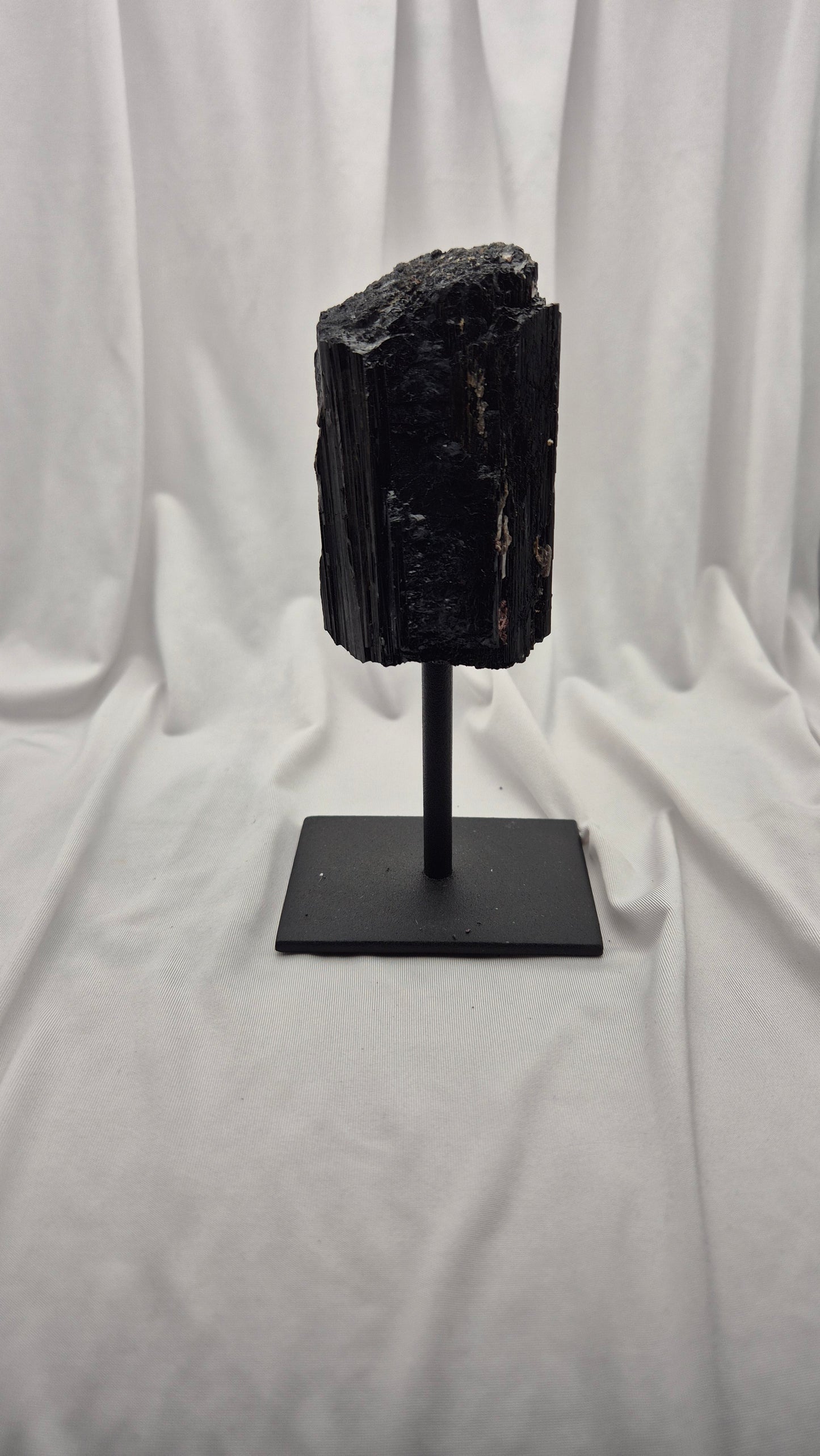 A black mineral or fossil specimen mounted on a black metal stand, photographed against a draped white fabric backdrop.