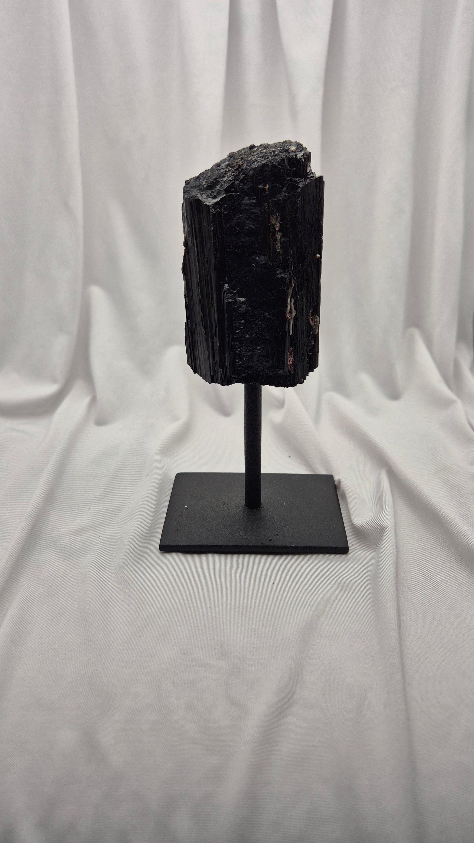 A black mineral or fossil specimen mounted on a black metal stand, photographed against a draped white fabric backdrop.