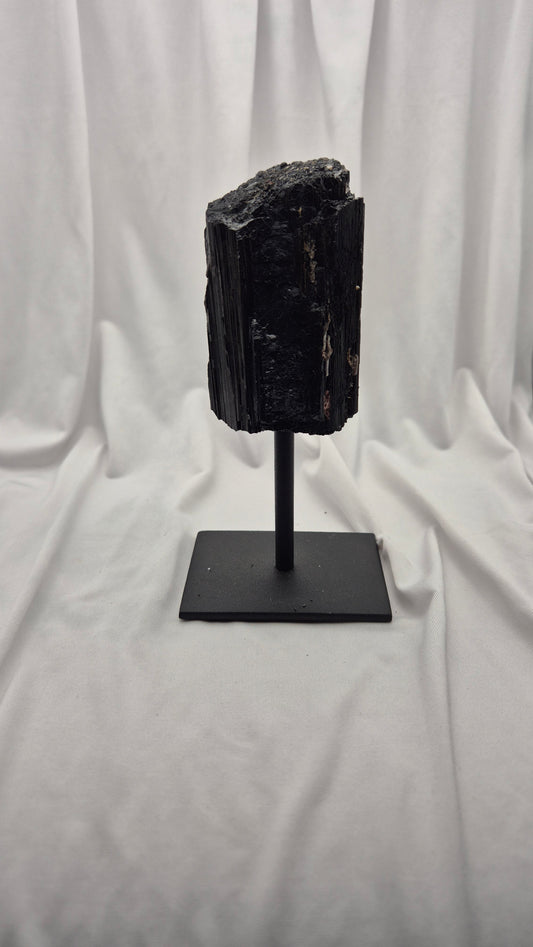A black mineral or fossil specimen mounted on a black metal stand, photographed against a draped white fabric backdrop.