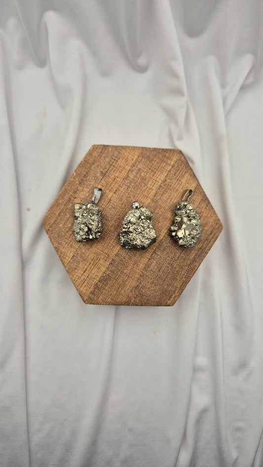 Three small pyrite pendants with silver-toned loops are displayed on a hexagonal wooden block over a draped white fabric background.