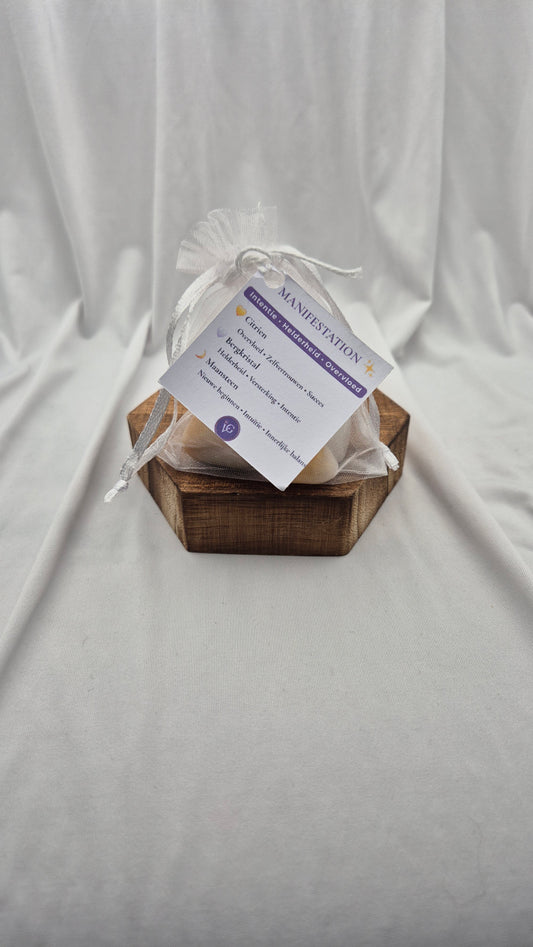 A small white sheer drawstring pouch with a printed tag sits on a hexagonal wooden tray against a draped white fabric backdrop.