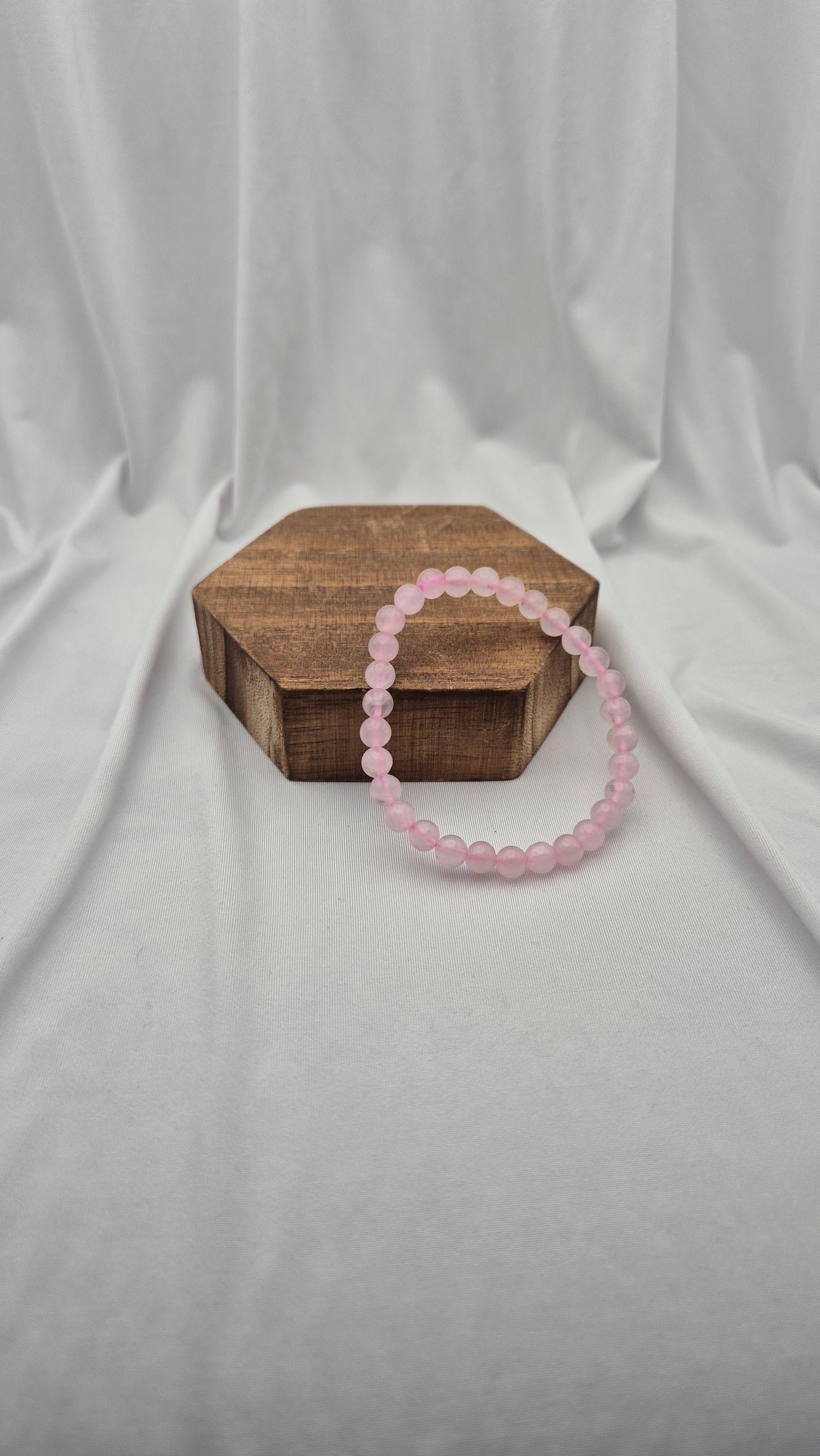 A pink beaded bracelet resting on a small hexagonal wooden box against a draped white fabric backdrop.
