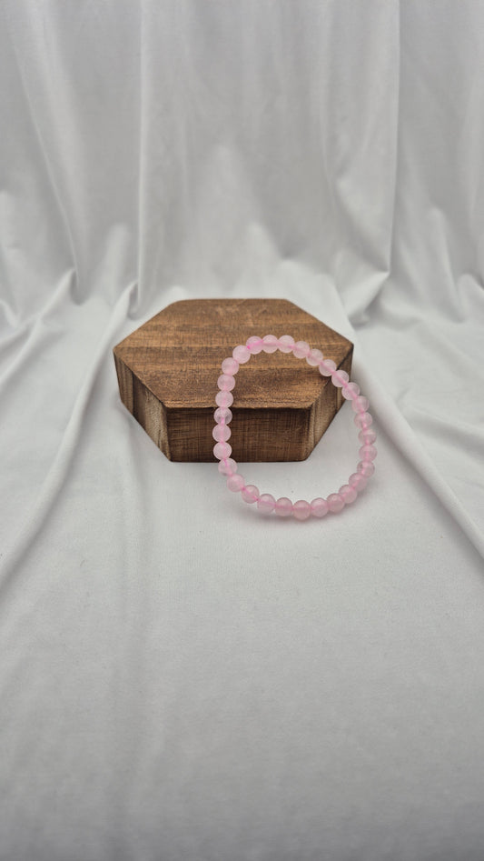 A pink beaded bracelet resting on a small hexagonal wooden box against a draped white fabric backdrop.