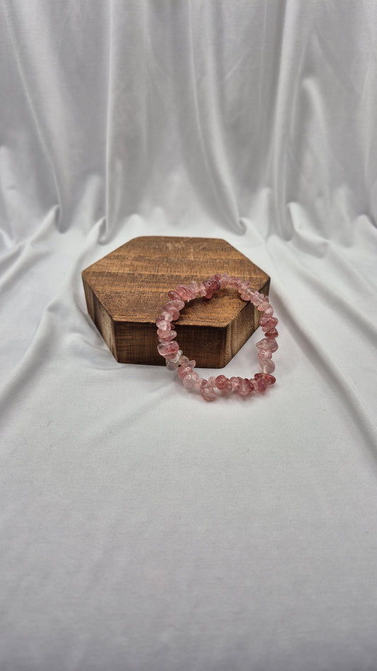 A pink beaded stretch bracelet made of faceted crystal-like beads, displayed on a small hexagonal wooden box against a draped white fabric backdrop.
